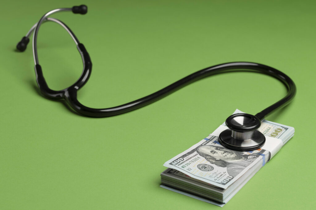 A photo of a stethoscope against a green background. It is resting on top of a stack of $100 bills.