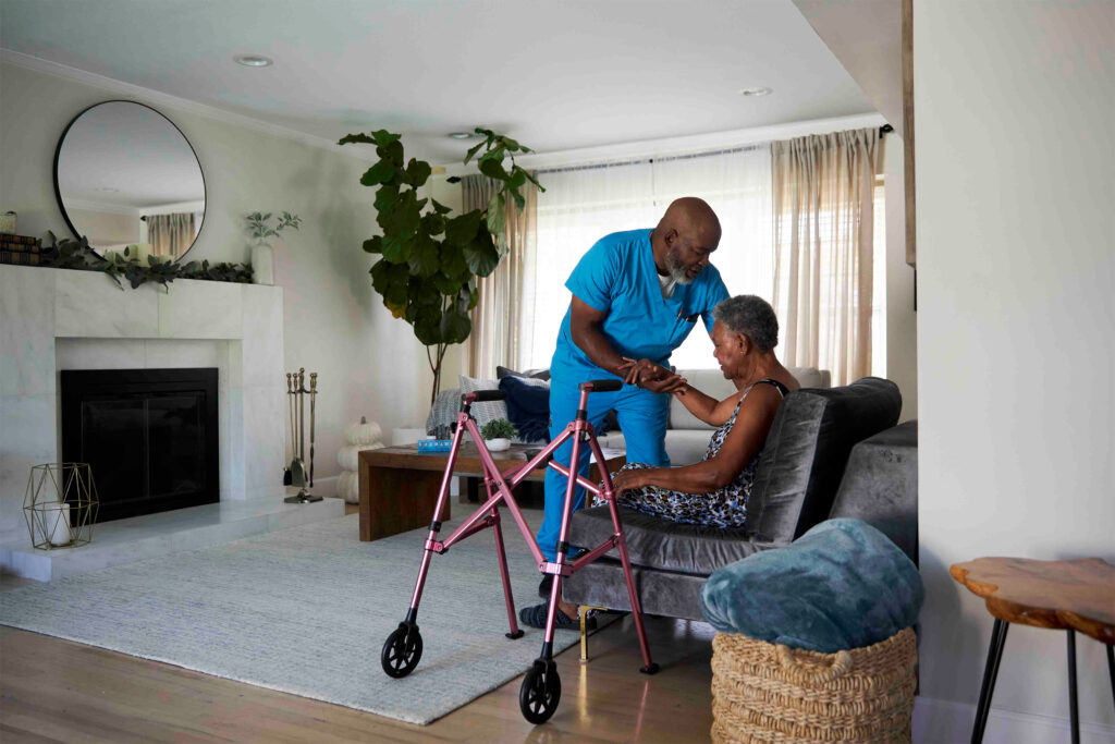 A photo of a home health aide helping an older woman sit down.