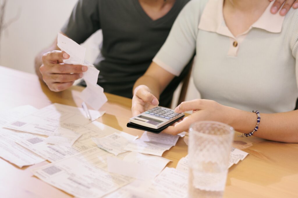 A man and woman seated at a table with papers, bills, receipts, and a calculator in front of them