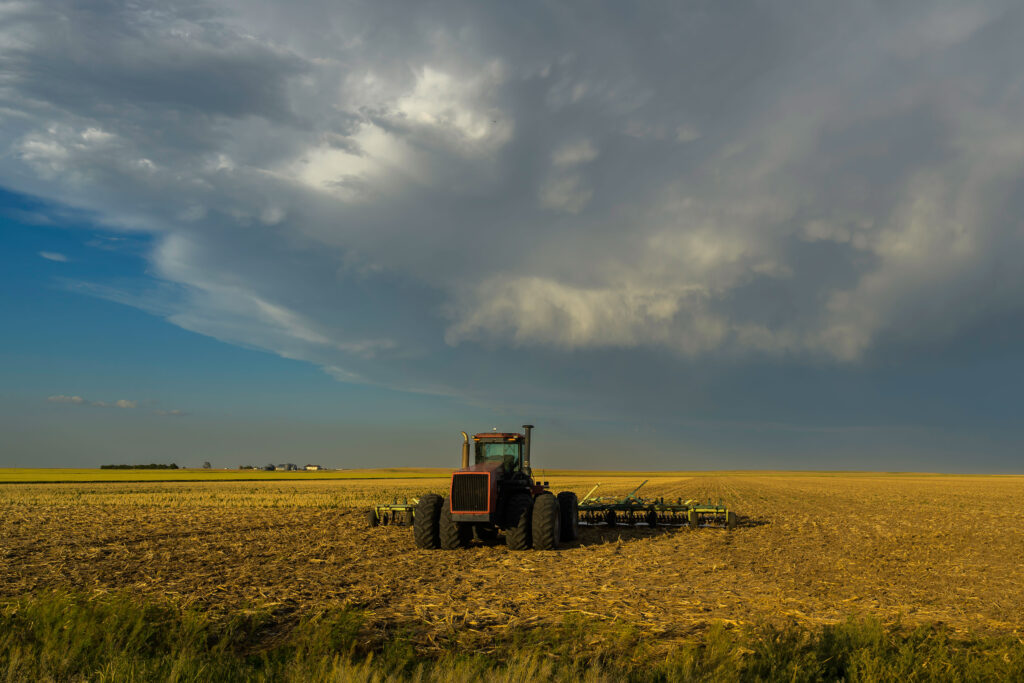A tractor is parked in a field. Dark clouds are moving overhead.
